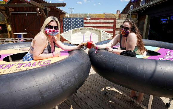 볼티모어의 트레이시 샌드리지와 줄리 브라운이 23일(현지시간) 미국 메릴랜드주 오션시티에서 피시 테일즈 바 앤 그릴이 코로나19 사회적 거리를 위해  ‘범퍼 테이블’을 고안해 재개장 해, 건배를 하며 포즈를 취하고 있다. 로이터 연합뉴스