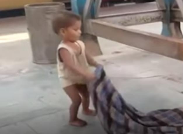 담요를 흔들어 엄마를 깨우려는 인도 기차역의 한 아기.  SNS 영상 캡처/연합뉴스