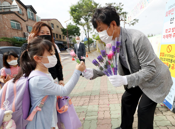 경기 부천지역 특수학교, 유치원, 초·중·고등학교(고3 제외) 등교 수업이 시작된 11일 오전 경기도 부천시 송내동 솔안초등학교에서 한 교사가 처음 입학하는 학생에게 꽃을 선물하며 축하고 있다. 2020.6.11  연합뉴스