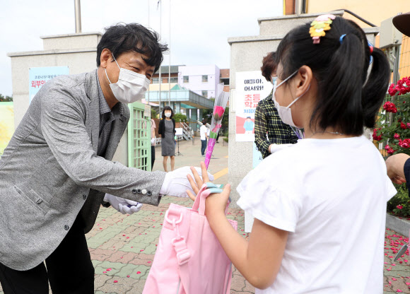 경기 부천지역 특수학교, 유치원, 초·중·고등학교(고3 제외) 등교 수업이 시작된 11일 오전 경기도 부천시 송내동 솔안초등학교에서 한 교사가 처음 입학하는 학생에게 꽃을 선물하며 축하고 있다. 2020.6.11  연합뉴스