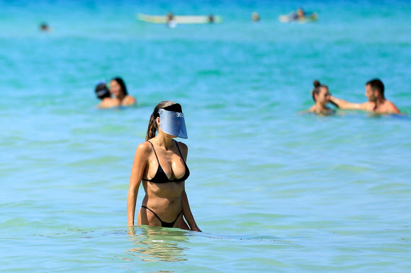 미국 플로리다 주민이 10일(현지시간) 코로나19 여파로 3개월여 문을 닫았다 재개방한 마이애미 비치  바닷가에서 방역모자를 쓰고 수영을 즐기고 있다. 게티/AFP 연합뉴스