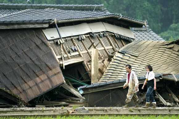한 커플이 5일(현지시간) 일본 남서부 구마모토현 쿠마마 마을에서 홍수로 피해를 입은 집 앞을 걷고 있다. 쿠마모토 지역에 폭우가 내려 홍수와 산사태가 발생했으며 수십 명이 여전히 집과 다른 시설에 발이 묶였다. AP 연합뉴스