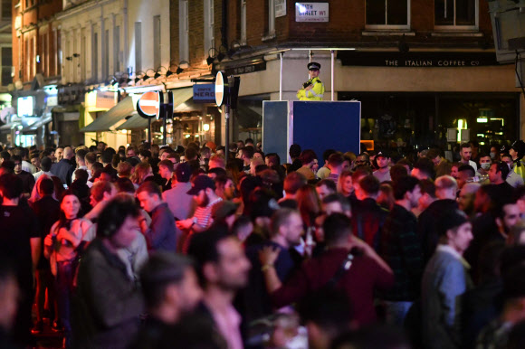 4일(현지시간) 영국 런던 소호지구에서 유흥객들로 넘쳐나는 거리를 경찰관이 내려다보고 있다. 신종 코로나바이러스 감염증(코로나19) 사태로 지난 3월 말 문을 닫았던 영국의 펍과 카페, 레스토랑 등은 이날부터 일제히 영업을 재개했다. AFP 연합뉴스