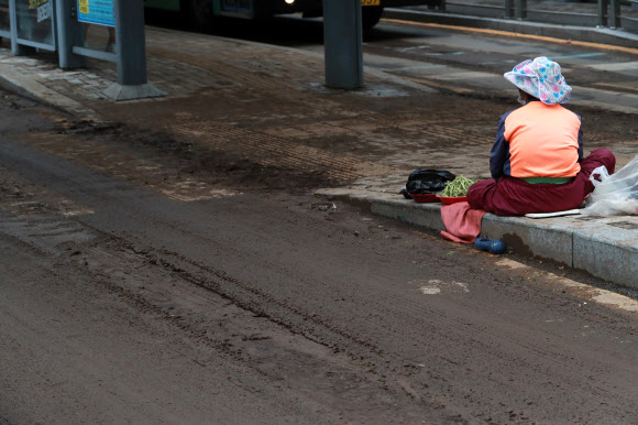 24일 오전 밤사이 내린 폭우로 진흙탕이 된 부산역 일대에서 한 할머니가 채소를 팔고 있다. 2020.7.24  연합뉴스