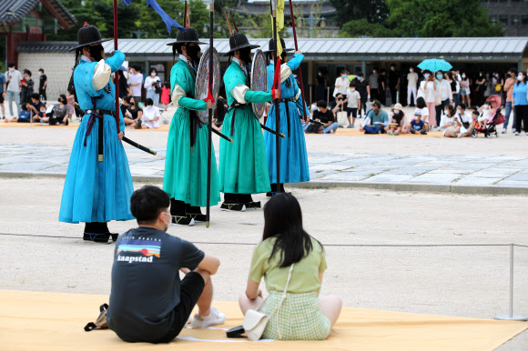신종 코로나바이러스 감염증(코로나19)으로 문을 닫았던 수도권 문화시설들이 재개관한 뒤 첫 주말을 맞은 26일 서울 종로구 경복궁을 찾은 시민들이 거리를 두고 앉아 수문장 교대 의식을 관람하고 있다. 2020.7.26  연합뉴스