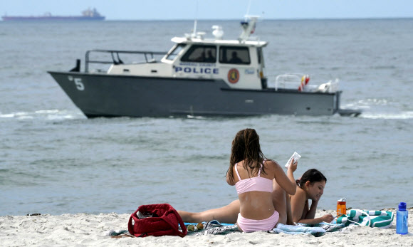29일(현지시간) 미국 뉴욕 리도 해변의 니커슨 비치 파크에 나소 카운티 경찰 해병대 보트가 순찰하는 가운데 시민들이 휴식을 취하고 있다. AFP 연합뉴스