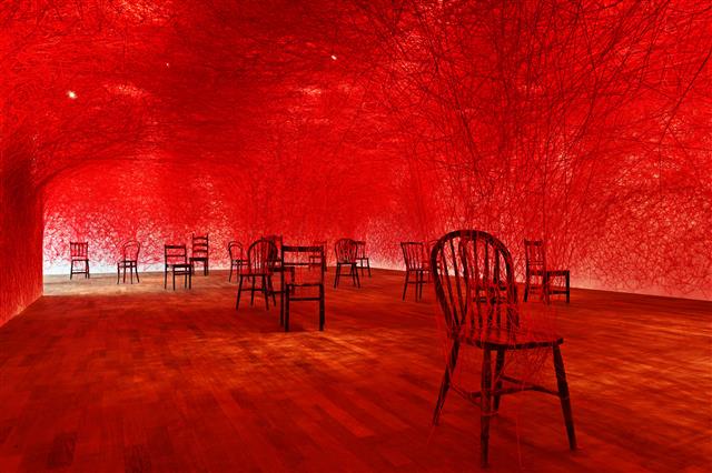 붉은 실로 서른 개 의자와 전시장 삼면을 촘촘히 연결한 시오타 치하루의 대형 설치작품 ‘비트윈 어스’는 대면 접촉이 제한되는 코로나 시대에 사회적 관계맺기의 의미를 되묻는다. 가나아트 제공