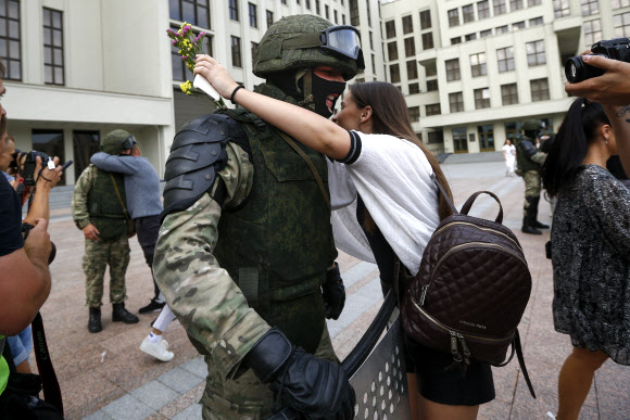한 참가자가 14일(현지시간) 벨로루시 민스크 독립광장 정부청사 근처에서 경찰의 폭력에 항의하고 대통령 선거 결과를 거부하기 위한 반대 시위 도중 경계를 서고 있는 벨라루시 내무부 부대원을 포옹하고 있다. AP 연합뉴스