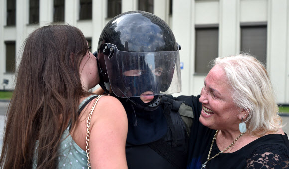 두 여성이 14일(현지시간) 벨로루시 민스크 독립광장 정부청사 근처에서 경찰의 폭력에 항의하고 대통령 선거 결과를 거부하기 위한 반대 시위 도중 경계를 서고 있는 벨라루시 내무부 부대원을 포옹하고 있다. AFP 연합뉴스