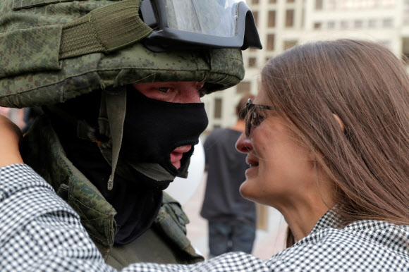 한 참가자가 14일(현지시간) 벨로루시 민스크 독립광장 정부청사 근처에서 경찰의 폭력에 항의하고 대통령 선거 결과를 거부하기 위한 반대 시위 도중 경계를 서고 있는 벨라루시 내무부 부대원을 포옹하고 있다. 로이터 연합뉴스