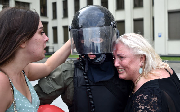 두 여성이 14일(현지시간) 벨로루시 민스크 독립광장 정부청사 근처에서 경찰의 폭력에 항의하고 대통령 선거 결과를 거부하기 위한 반대 시위 도중 경계를 서고 있는 벨라루시 내무부 부대원을 포옹하고 있다. AFP 연합뉴스