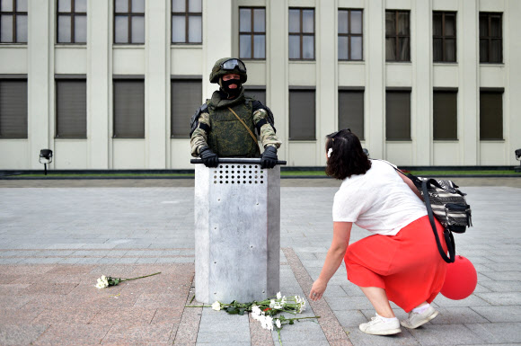 한 참가자가 14일(현지시간) 벨로루시 민스크 독립광장 정부청사 근처에서 경찰의 폭력에 항의하고 대통령 선거 결과를 거부하기 위한 반대 시위 도중 경계를 서고 있는 벨라루시 내무부 부대원 앞에 꽃을 놓고 있다. AFP 연합뉴스
