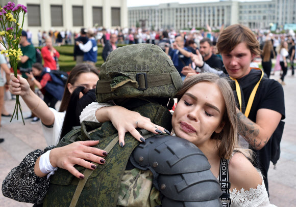 한 참가자가 14일(현지시간) 벨로루시 민스크 독립광장 정부청사 근처에서 경찰의 폭력에 항의하고 대통령 선거 결과를 거부하기 위한 반대 시위 도중 경계를 서고 있는 벨라루시 내무부 부대원을 포옹하고 있다. AFP 연합뉴스