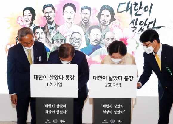 문재인 대통령과 김정숙 여사가 15일 서울 중구 동대문디자인플라자에서 열린 제75주년 광복절 경축식에 참석해 ‘대한이 살았다’ 통장 1호와 2호 가입 서명을 하고 있다. 왼쪽은 윤종규 KB금융지주 회장. 2020.08.15.청와대사진기자단/매일경제 이충우기자