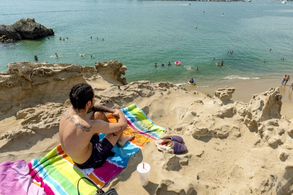 한 남성이 18일(현지시간) 미국 캘리포니아 뉴포트 비치의 코로나 델 마르에 있는 파이러츠 코브가 내려다보이는 바위에서 해변에서 더위를 식히는 것을 지켜보고 있다. 국립기상청은 남부 캘리포니아에 폭염 경보를 발령했다. AP 연합뉴스