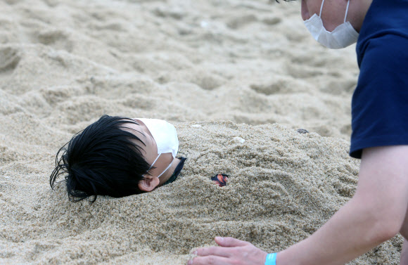 해양수산부가 코로나19 재확산에 따라 전국의 해수욕장을 긴급 폐장하기로 한 22일 강원 강릉 경포해수욕장에서 피서객이 마스크를 쓰고 모래찜질을 하고 있다. 전국의 해수욕장은 이날 밤 12시부터 긴급 폐장한다. 2020.8.22  연합뉴스