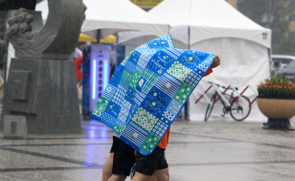 22일 오후 속초지역에 천둥을 동반한 강한 소나기가 쏟아지자 속초해수욕장을 찾았던 피서객들이 돗자리를 우산대용으로 쓰고 이동하고 있다.  2020.8.22  연합뉴스