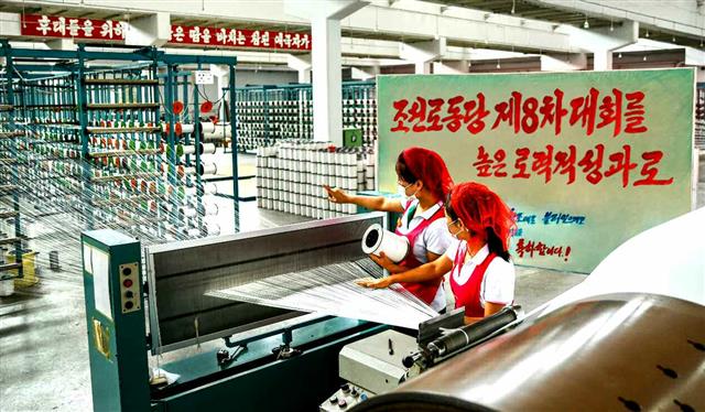 내년 1월 개최 예정인 북한 노동당 제8차 대회를 앞두고 당 기관지 노동신문은 “높은 정치적 열의와 빛나는 노력적 성과로 당대회를 맞이하자”라고 24일 독려했다. 사진은 작업 중인 김정숙평양방직공장 노동자들로 뒤편에 ‘당 제8차 대회를 높은 노력적 성과로’라고 적힌 선전물이 보인다.   평양 노동신문=뉴스1