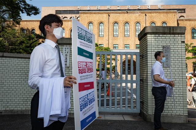 대한전임의협의회 소속 전임의들이 24일 서울 종로구 서울대 의과대학 입구에서 의사 가운을 벗어 들고 정부의 의과대학 정원 확대 등에 반대하는 손팻말을 들고 있다.  대한전임의협의회는 24일부터 차례로 단체행동에 돌입해 26일부터 전국의 모든 병원에서 전임의 파업에 돌입하겠다고 밝혔다. 2020.8.24 뉴스1