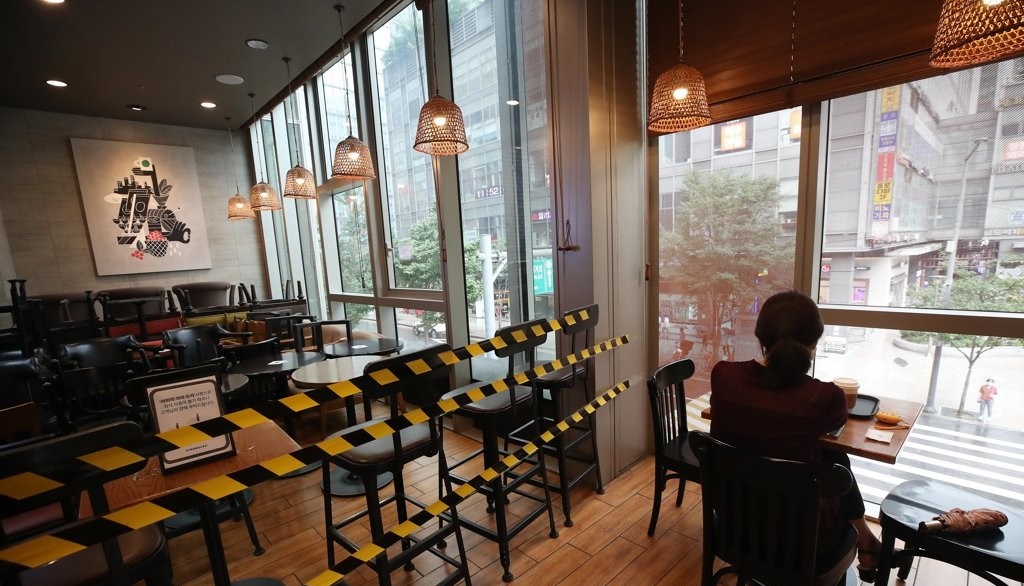 사회적 거리두기 2단계가 조치 중인 지난 21일 서울의 한 카페의 이용객 곁에 사용하지 않는 테이블과 의자가 쌓여있는 모습. 사진=연합뉴스