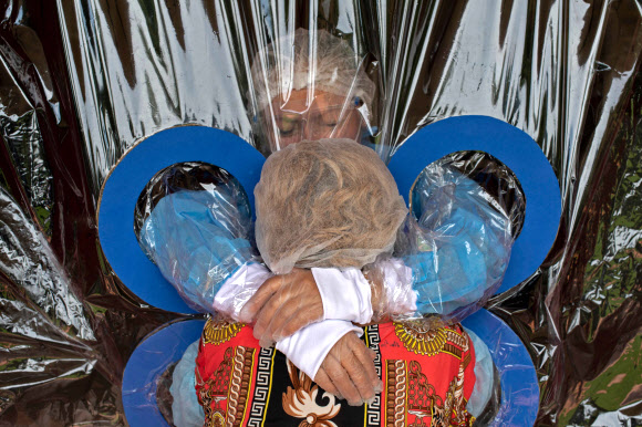 코로나19 대유행 속에 마리아 에르난데스가 11일(현지시간) 산살바도르의 호가르 자딘 드 로스 아부엘리토스 요양원에서 투명 커튼을 통해 이모를 껴안고 있다. 노인과 의사 루이스 버뮤즈에 따르면, 노인들이 코로나19에 감염될 위험 없이 친척들에게 포옹을 받을 수 있는 일종의 커튼을 사용하는 것은 우울증과 불안을 피하기 위한 조치라고 한다. AFP 연합뉴스