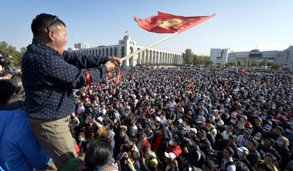 키르기스스탄의 총선 부정에 항의해 5일(현지시간) 수도 비슈케크의 의회 의사당 앞에 모여 있던 야권 지지자들을 향해 한 남성이 국기를 흔들며 독려하고 있다. 비슈케크 AP 연합뉴스 