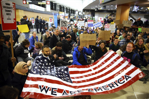 2017년 1월 시애틀 공항에서 여러 인종의 사람들이 모여 “우리는 미국이다”라고 적힌 성조기를 들고 있다. AP