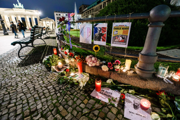 지난 16일(이하 현지시간) 프랑스 파리 근교 중학교 근처 거리에서 참수 살해된 역사 교사 사뮈엘 파티를 추모하는 촛불들과 격려 메시지, 헌화된 꽃들이 19일 독일 베를린의 브란덴부르크 문 근처 프랑스 대사관 앞에 놓여져 있다. 베를린 EPA 연합뉴스 