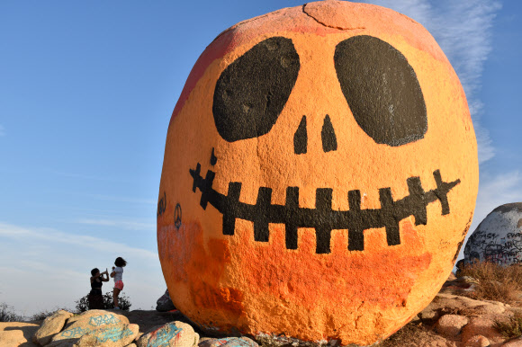 18일(현지시간) 미국 캘리포니아주 리버사이드 카운티 노르코의 한 언덕 위에 자리한 호박 바위 앞에서 사람들이 기념촬영을 위해 포즈를 취하고 있다. 신화 연합뉴스