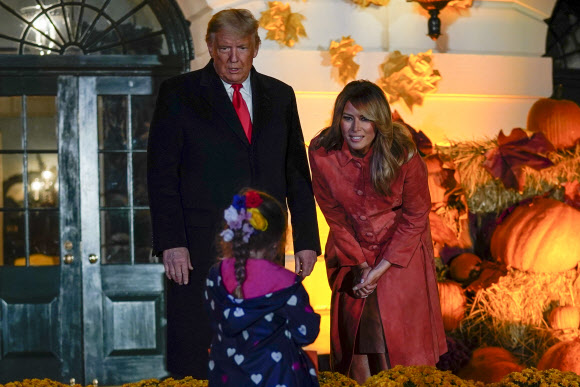 25일(현지시간) 도널드 트럼프 대통령과 영부인 멜라니아 여사가 백악관에서 열린 핼러윈 파티에서 마스크를 쓰지 않은 채 아이를 맞고 있다. AP