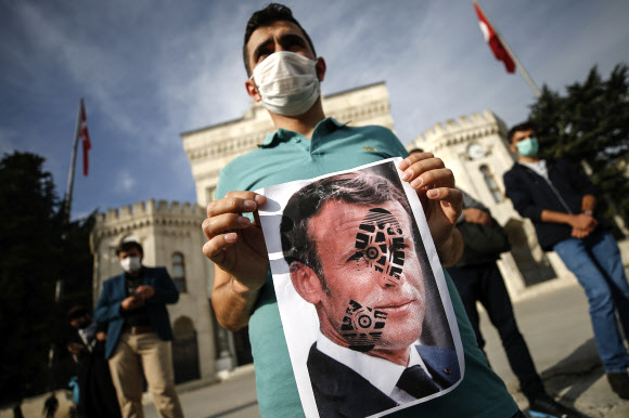 프랑스와 이슬람 국가 간 갈등이 확산일로인 가운데 25일(현지시간) 터키 수도 이스탄불의 반프랑스 시위에 참가한 청년이 신발 자국이 찍힌 에마뉘엘 마크롱 프랑스 대통령의 얼굴 사진을 들어 보이고 있다. 이스탄불 AP 연합뉴스