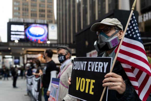 미국 뉴욕 맨해튼에서 대통령 선거 사전 투표가 시작된 지난 24일(현지시간) 투표소로 사용되는 매디슨 스퀘어가든 앞에서 마스크를 쓴 시위대원이 “모든 투표를 집계하라”는 팻말을 들어 보이고 있다. 로이터 자료사진 연합뉴스 