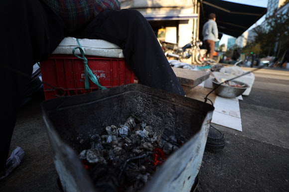 아침 기온이 5도 이하로 추운 날씨를 보인 3일 오전 서울 중구 새벽시장에서 상인이 거의 다 타들어간 장작불에 몸을 녹이고 있다. 2020.11.3  연합뉴스