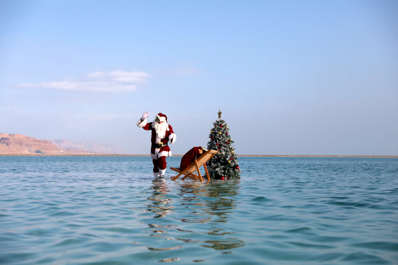 산타클로스 의상을 입은 한 남성이 15일(현지시간) 이스라엘 아인 보크크 인근 사해 성지의 소금 위에서 이스라엘 관광부가 주최한 크리스마스 맞이 비디오 촬영을 위해 크리스마스 트리 옆에 앉아 포즈를 취하고 있다. 이스라엘 관광부는 코로나19로 인해 관광이 심각한 타격을 입었다고 밝혔고 이스라엘은 코로나19 위기 속에서 휴가철을 준비하고 있다. EPA 연합뉴스