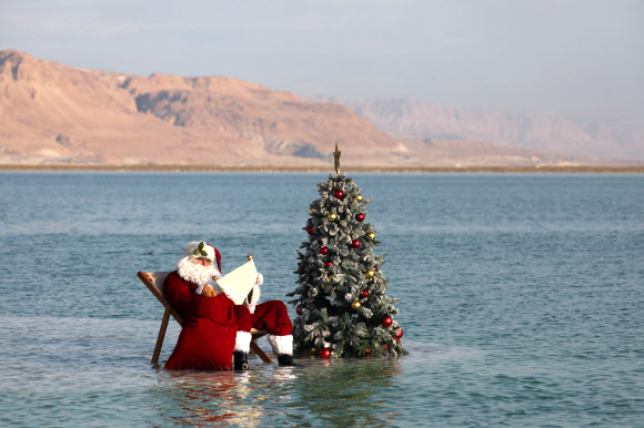 산타클로스 의상을 입은 한 남성이 15일(현지시간) 이스라엘 아인 보크크 인근 사해 성지의 소금 위에서 이스라엘 관광부가 주최한 크리스마스 맞이 비디오 촬영을 위해 크리스마스 트리 옆에 앉아 포즈를 취하고 있다. 이스라엘 관광부는 코로나19로 인해 관광이 심각한 타격을 입었다고 밝혔고 이스라엘은 코로나19 위기 속에서 휴가철을 준비하고 있다. EPA 연합뉴스