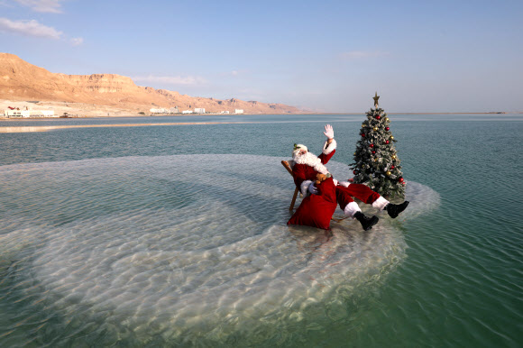 산타클로스 의상을 입은 한 남성이 15일(현지시간) 이스라엘 아인 보크크 인근 사해 성지의 소금 위에서 이스라엘 관광부가 주최한 크리스마스 맞이 비디오 촬영을 위해 크리스마스 트리 옆에 앉아 포즈를 취하고 있다. 이스라엘 관광부는 코로나19로 인해 관광이 심각한 타격을 입었다고 밝혔고 이스라엘은 코로나19 위기 속에서 휴가철을 준비하고 있다. EPA 연합뉴스