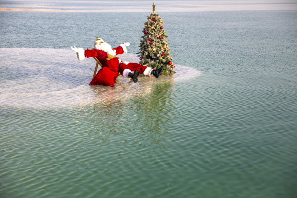 산타클로스 의상을 입은 한 남성이 15일(현지시간) 이스라엘 아인 보크크 인근 사해 성지의 소금 위에서 이스라엘 관광부가 주최한 크리스마스 맞이 비디오 촬영을 위해 크리스마스 트리 옆에 앉아 포즈를 취하고 있다. 이스라엘 관광부는 코로나19로 인해 관광이 심각한 타격을 입었다고 밝혔고 이스라엘은 코로나19 위기 속에서 휴가철을 준비하고 있다. AP 연합뉴스