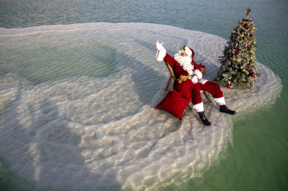 산타클로스 의상을 입은 한 남성이 15일(현지시간) 이스라엘 아인 보크크 인근 사해 성지의 소금 위에서 이스라엘 관광부가 주최한 크리스마스 맞이 비디오 촬영을 위해 크리스마스 트리 옆에 앉아 포즈를 취하고 있다. 이스라엘 관광부는 코로나19로 인해 관광이 심각한 타격을 입었다고 밝혔고 이스라엘은 코로나19 위기 속에서 휴가철을 준비하고 있다. AP 연합뉴스