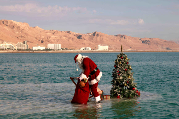 산타클로스 의상을 입은 한 남성이 15일(현지시간) 이스라엘 아인 보크크 인근 사해 성지의 소금 위에서 이스라엘 관광부가 주최한 크리스마스 맞이 비디오 촬영을 위해 크리스마스 트리 옆에 앉아 포즈를 취하고 있다. 이스라엘 관광부는 코로나19로 인해 관광이 심각한 타격을 입었다고 밝혔고 이스라엘은 코로나19 위기 속에서 휴가철을 준비하고 있다. AFP 연합뉴스