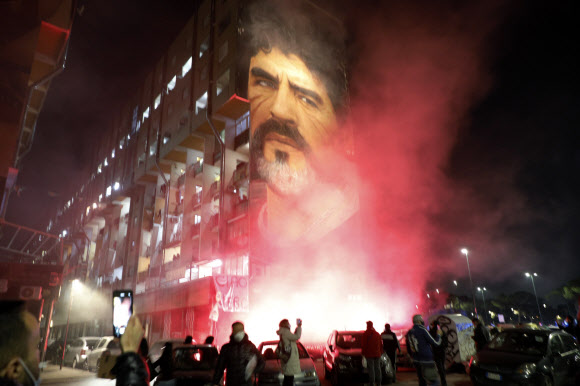 사람들이 25일(현지시간) 이탈리아 나폴리에서 축구 전설 디에고 마라도나의 벽화를 환하게 밝히며 모여 있다. AP 연합뉴스