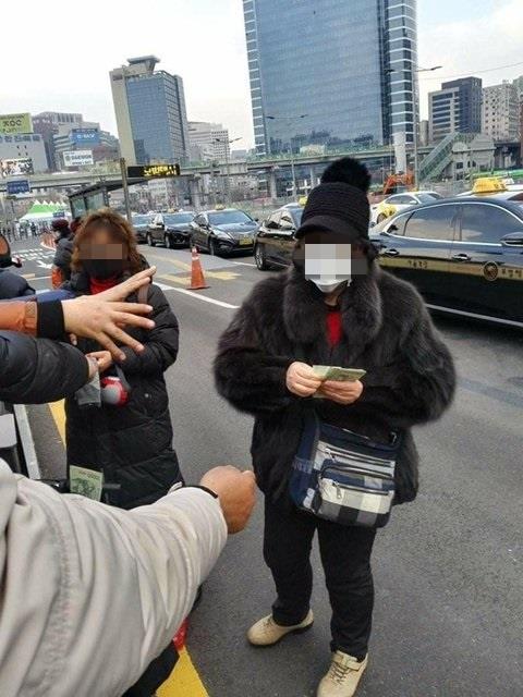 22일 오후 서울 용산구 서울역 광장에서 교회 관계자들이 노숙인 등에게 현금 1만원을 나눠주고 있다. 트위터 캡처