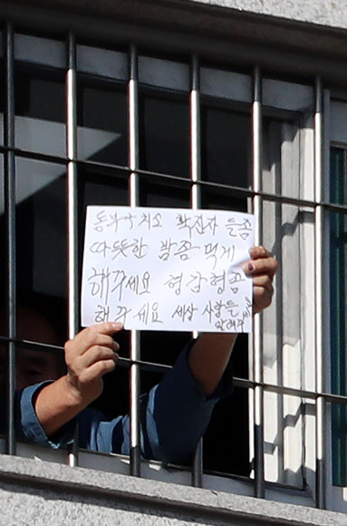 6일 오후 서울 송파구 동부구치소에서 한 수용자가 ‘확진자들 따뜻한 밥 좀 먹게해주세요’라고 쓴 종이를 창문 밖 취재진에게 내보이고 있다. 법무부는 이날 동부구치소 수용자 66명이 추가로 확진 판정을 받았다고 밝혔다. 2021.1.6  연합뉴스
