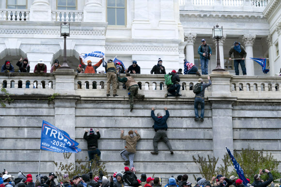 지난 6일 도널드 트럼프 미국 대통령의 극렬 지지자들이 워싱턴DC 국회의사당에 난입하기 위해 담벼락을 오르고 있다. 워싱턴 AP 연합뉴스