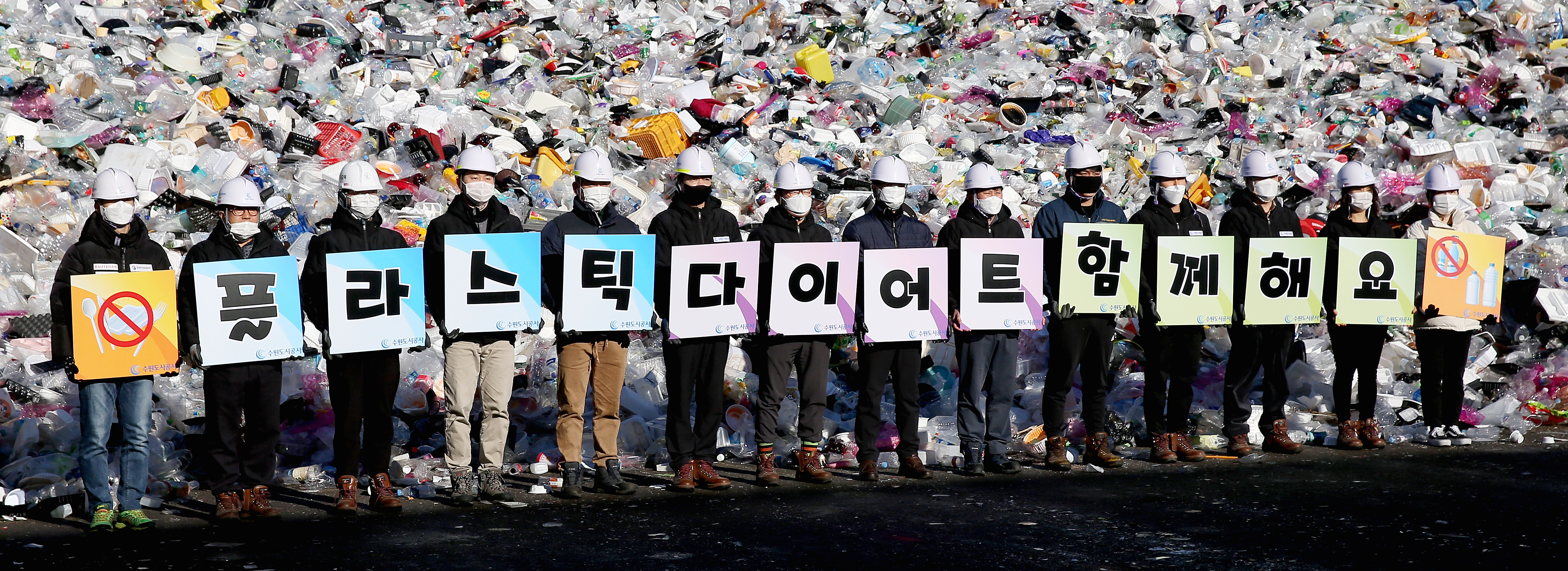 19일 오전 수원시자원순환센터 플라스틱 야외적치장에서 수원도시공사 임직원들이 ‘고고 릴레이’ 캠페인의 일환으로 ‘플라스틱 다이어트 함께해요’란 글이 새겨진 피켓을 선보이는 퍼포먼스를 하고 있다.  수원도시공사 제공 