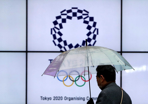 23일 한 도쿄시민이 우산을 들고 도쿄올림픽 로고가 표시된 전광판 앞을 지나고 있다. 2021.1.23 로이터 연합뉴스