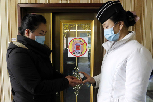 5일(현지시간) 북한 평양의 봉남국수집 종업원(오른쪽)이 마스크를 쓰고 식당으로 들어오는 손님의 손을 소독하고 있다. AP 연합뉴스