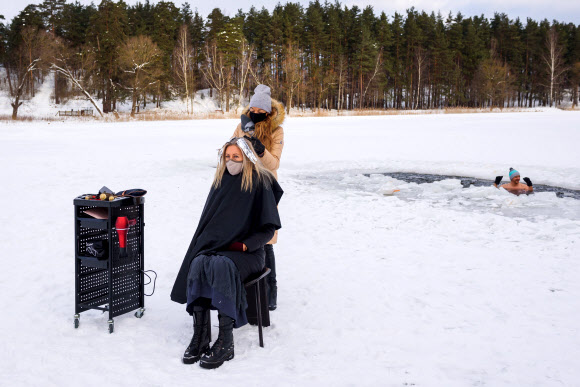 한 미용사가 15일(현지시간) 라트비아의 수도 리가 인근의 호숫가에서 손님의 머리카락을 자르고 있다. 이 미용사는 신종 코로나바이러스 감염증(코로나19) 여파로 미용실 영업이 금지되자 꽁꽁 얼어붙은 이곳 호숫가로 와 손님을 받았다. AFP 연합뉴스