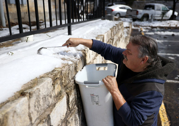 19일(현지시간) 미국 텍사스주 오스틴에서 한 시민이 급수가 중단되자 눈을 녹여 물을 사용하기 위해 쌓인 눈을 담고 있다. AFP 연합뉴스
