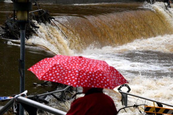 22일(현지시간) 기록적 폭우가 내린 호주 시드니에서 우산을 쓴 시민이 범람한 파라마타 강을 바라보고 있다. AFP 연합뉴스