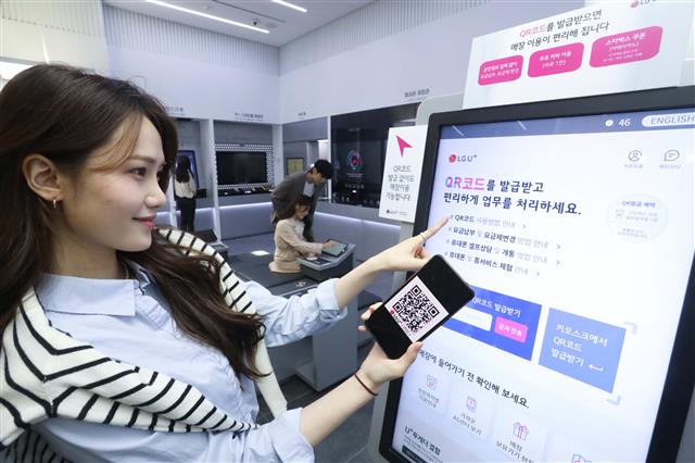 LG유플러스가 서울 종로 르메이르타워 1층에 마련한 무인 매장인 U+ 언택트스토어 1호점 웰컴 보드에서 모델이 QR코드를 발급받고 있는 모습. LG유플러스 제공